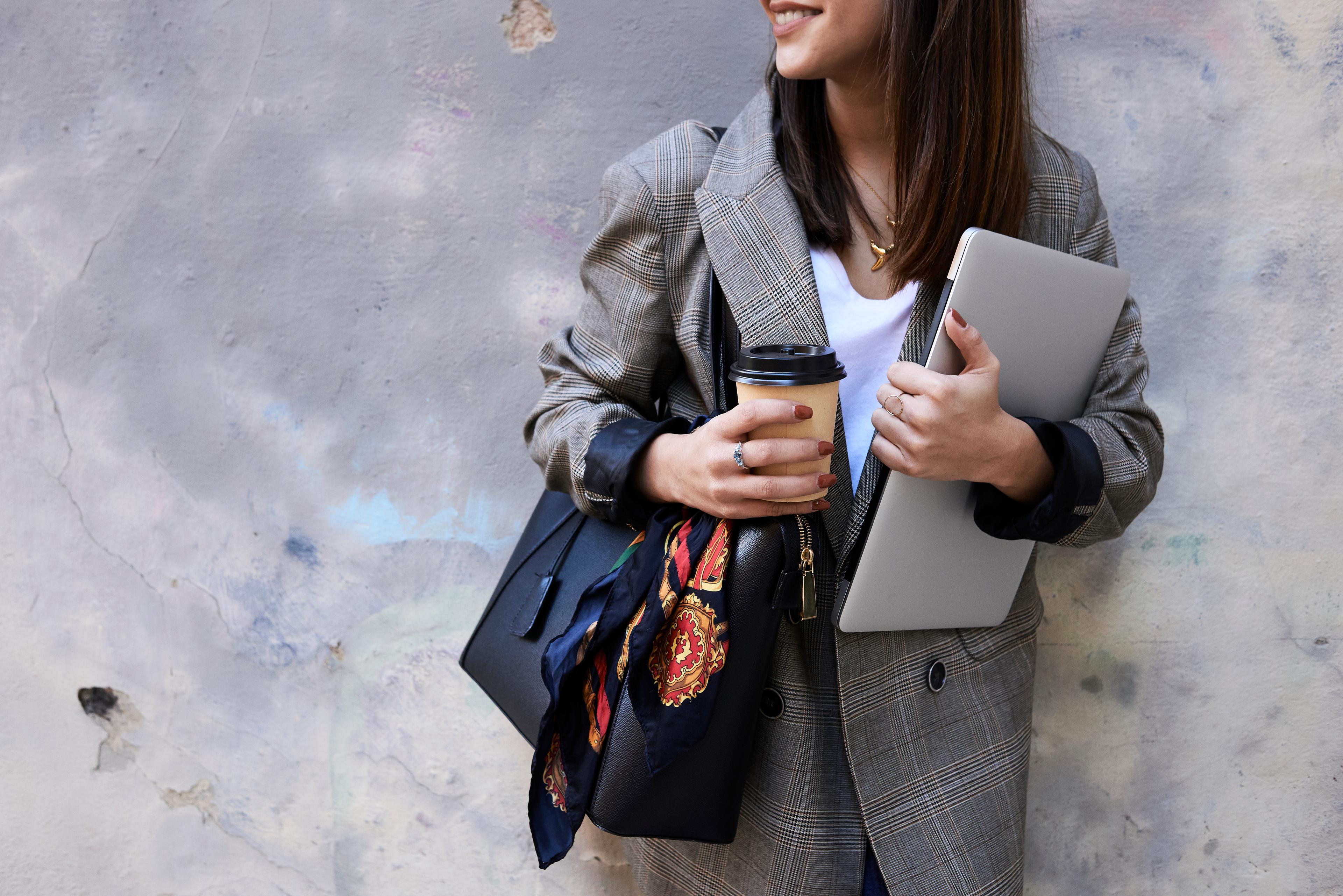 assistant smiling while holding a cup of coffee in one hand and a laptop in the other