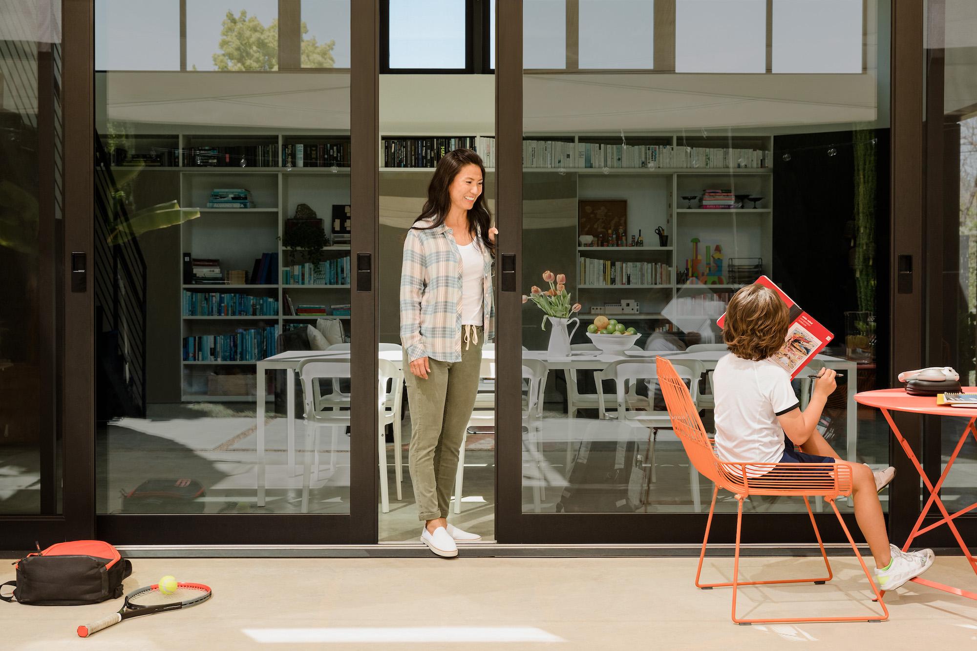 Yohana CEO stands between open glass doors looking out at a child on the patio, holding a book