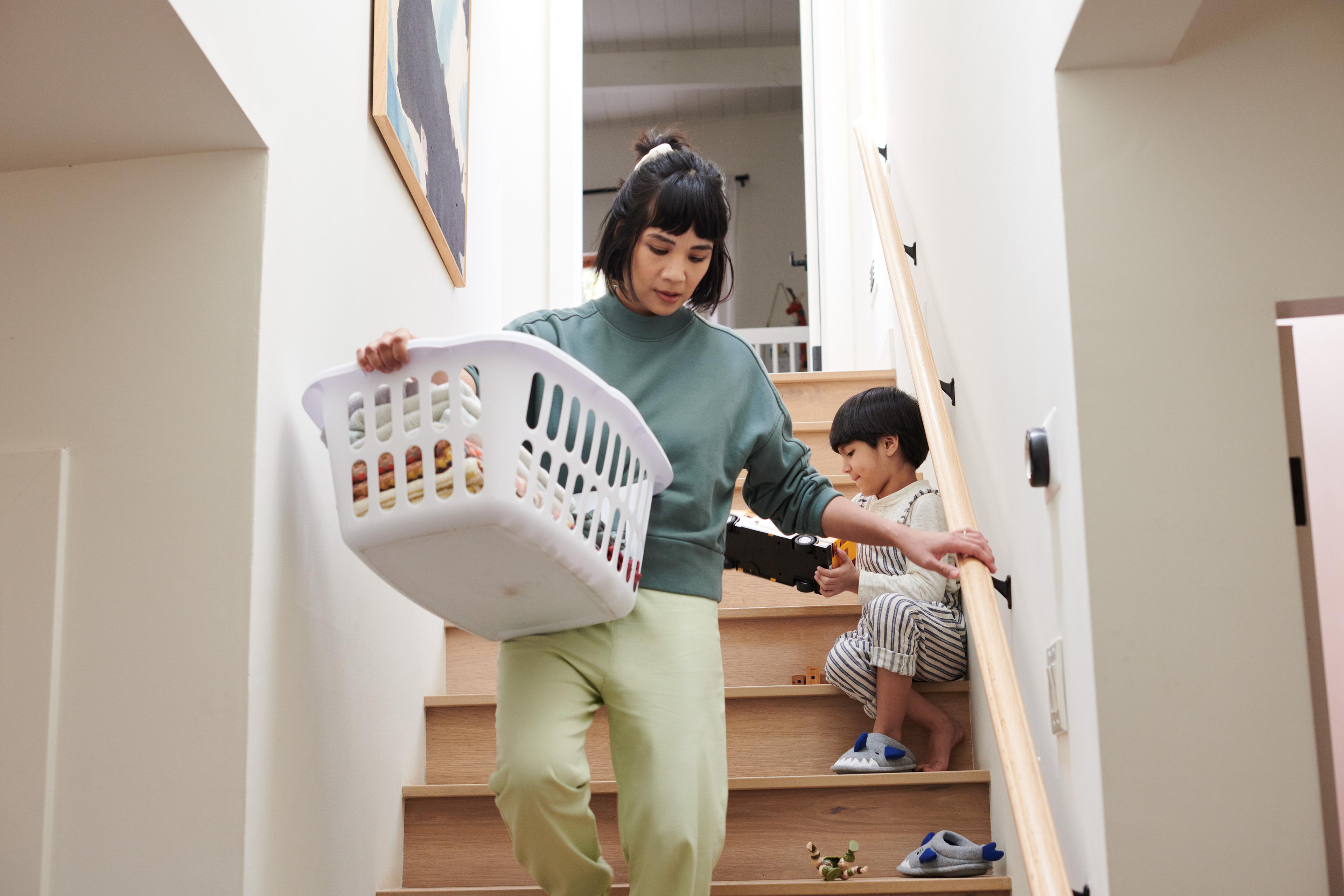 Woman walking down stairs with laundry basket past child playing with toys on the steps