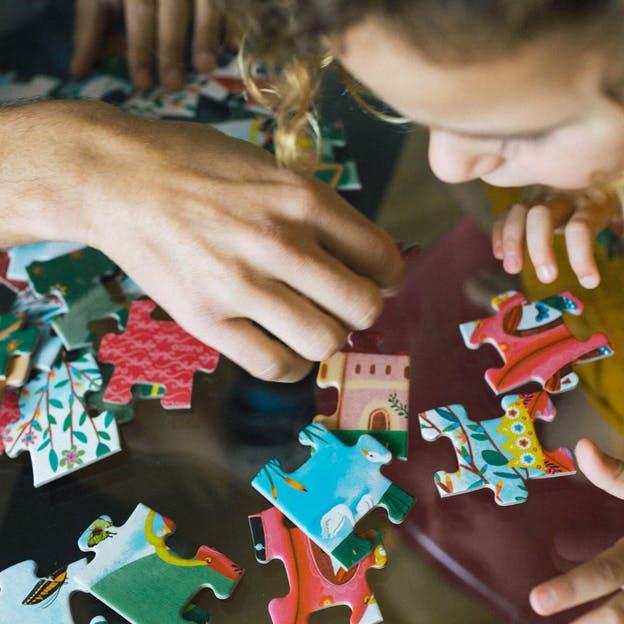 Close up of adult hands over puzzle pieces, with a child watching