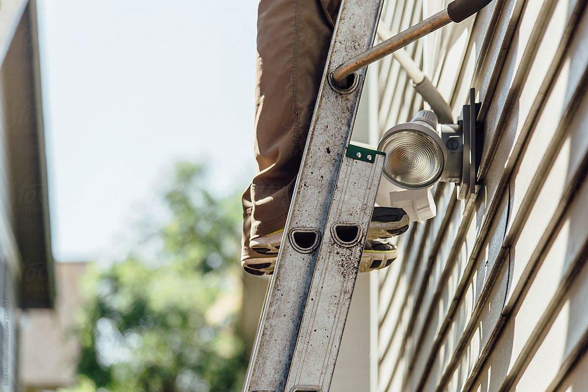 Close-up of a handyman’s feet on a ladder against exterior home siding