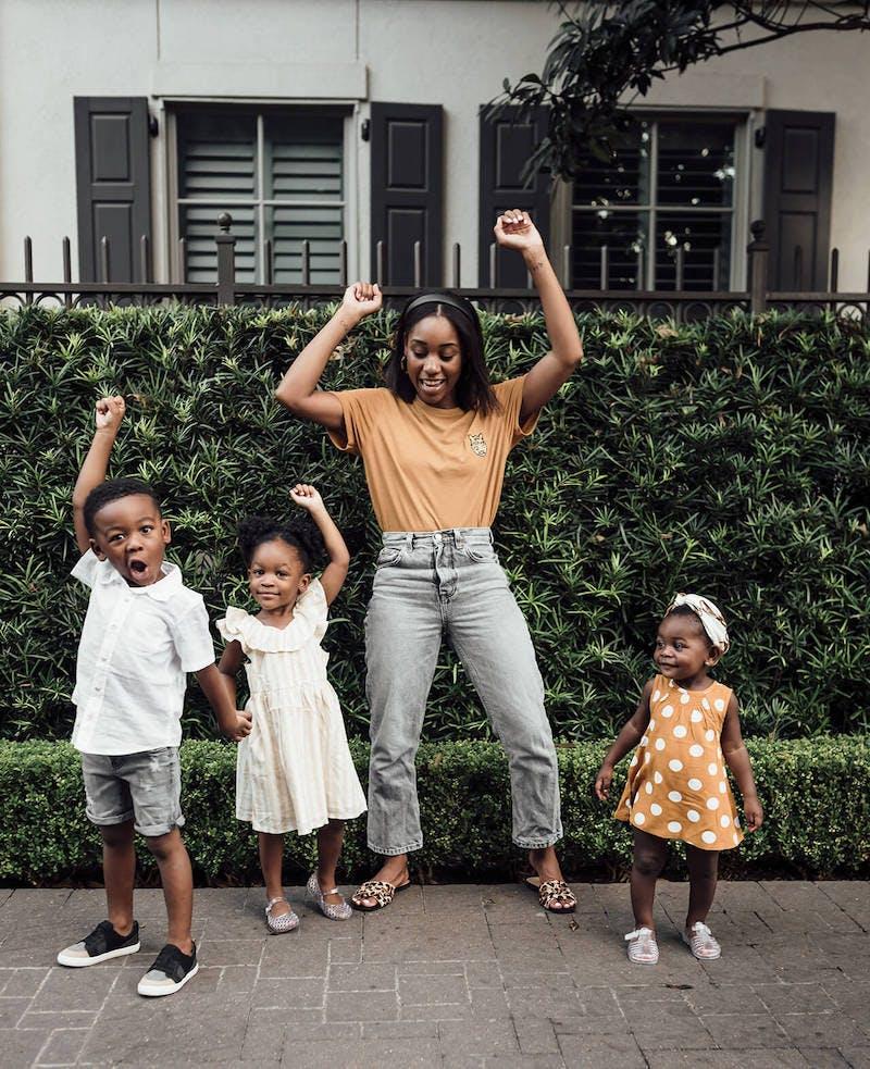 Woman and three children hold their arms in the air and make playful faces